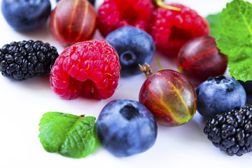 Close-up arrangement mixed, assorted berries including blackberries, strawberry, blueberry, raspberries and fresh leaf on white