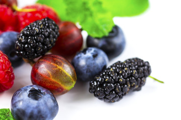 Close-up arrangement mixed, assorted berries including blackberries, strawberry, blueberry, raspberries and fresh leaf on white