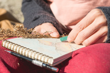 Close-up of a hand Girl artist paints a pastel in a notebook on nature in the mountains. Free creativity and freelancing