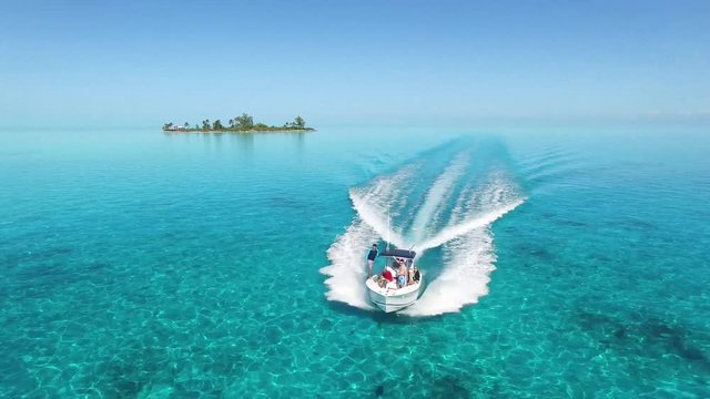 4K Aerial -- Boat Fly Over, Crystal Clear, Flat Calm Bahamian Waters, Deserted Island in background, Dynamic Camera Movement