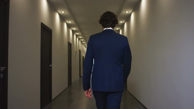 man walks along gently lit hotel hall with doors