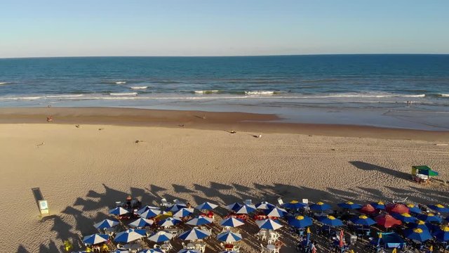 Umbrellas on the beach near the blue sea with waves and surfers in Aracaju, Brazil