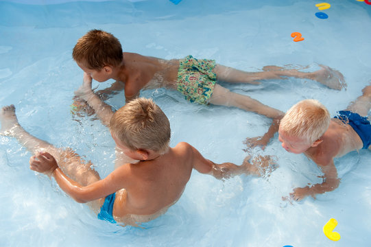 Two happy children play in swimming pool with plastic letters and numbers for bathroom. Brothers are happy together in warm water on sunny summer day. Concept of teaching games for preschoolers.