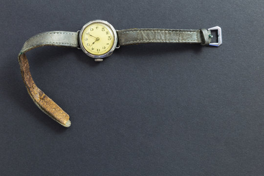 Closeup of a retro style yellow colored wristwatch with worn leather straps on black background.