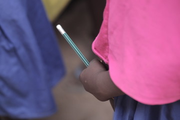 african education close up - macro photography of a black african school kid hand holding a pencil, outdoors  in the Gambia, Africa on a summer day