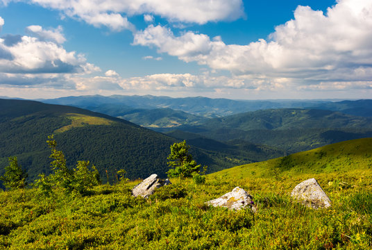 three boulders on grassy hillside of Runa mountain under the summer sky. fluffy clouds over the Polonina Carynska and Wielka Rawka mountain in the far distance
