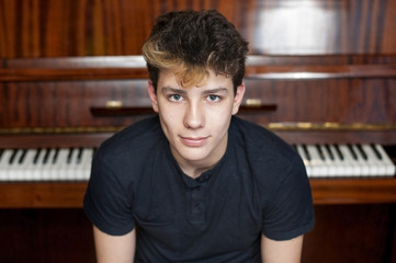 A cute teen smiles against a piano background. He had a good mood because he played well at the concert © Мар'ян Філь