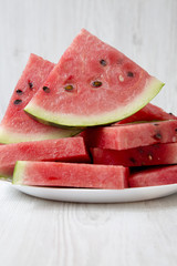 Many slices of ripe juicy watermelon on a round white plate, closeup. Side view.