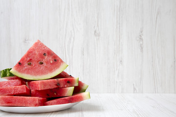 Many slices of ripe juicy watermelon on a round white plate with copy space, closeup. Side view.