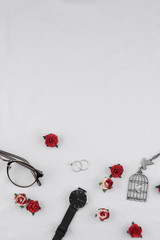 Eyeglasses, black watches, necklace and rings decorate with red rose paper flowers on white fabric with copy space