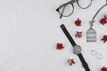 Eyeglasses, black watches, necklace and rings decorate with red rose paper flowers on white fabric with copy space