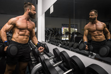 Hombre fuerte con grandes músculos entrenando con mancuernas  en el gimnasio. Ponerse en forma.