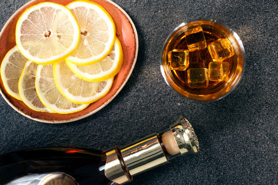 Stemware and bottle of whiskey,plate with sliced lemon on a stone background. Alcohol background