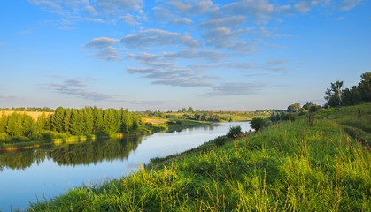 Fototapeta na wymiar Tranquil summer landscape with beautiful river,woods,fields and green hills.Sunny windless morning.