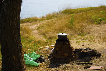 Bowler on a homemade stone hearth under a tree in the middle of grass and the sea. The concept of an ideal holiday in nature.