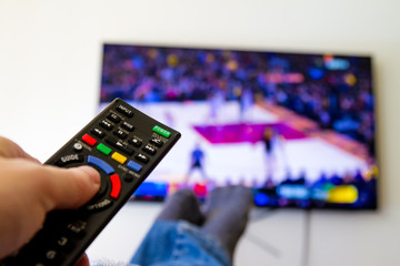 Close-up macro of man's hand with TV remote control watching a basketball game