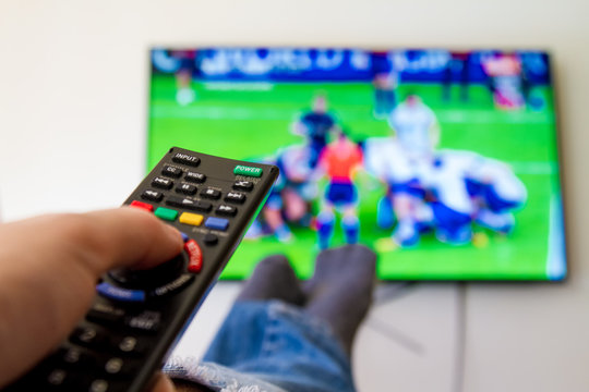 Close-up macro of man's hand with TV remote control watching a rugby match
