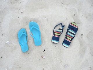 Fototapeta na wymiar Two pairs of flip flops in the sand on the beach 
