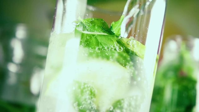 Slow motion beautiful bubbles on mint leaves rise up in a misted glass with ice and lemon