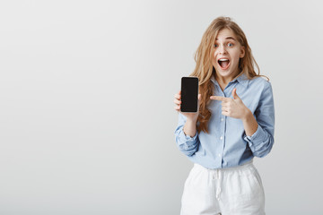 Girl won smartphone in lottery. Portrait of amazed charming young female in blue blouse showing...