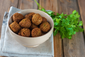 Falafel balls  in ceramic bowl and green fresh parsley on a wooden background. Falafel is a traditional Middle Eastern food, commonly served in a pita.