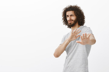 Portrait of cute bearded digusted guy in trendy outfit, bending backwards and pulling palms towards...