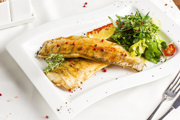 Baked fish fillet with lemon and fresh vegetables on white plate