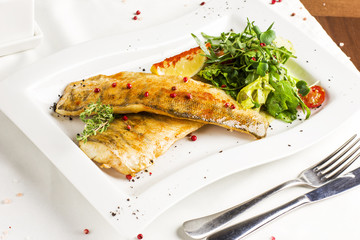 Baked fish fillet with lemon and fresh vegetables on white plate