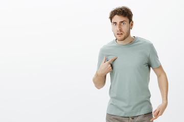 Portrait of shocked frustrated handsome european man in earrings, pointing at himself with index...