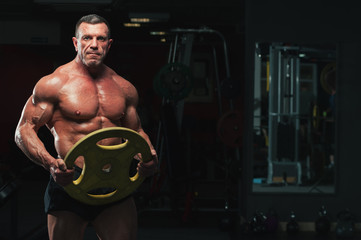 Fototapeta na wymiar High level bodybuilder with perfect relief body posing with heavy weights in hands. Strong mature man in the gym