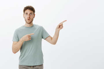 Studio shot of shocked amazed man hearing terrible rumor, discussing it and pointing right at person who told revelation, standing stunned and impressed, folding lips over gray background