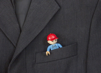 in the breast pocket of a dark black man's jacket in a light strip is a toy from the designer of a little man in a red cap