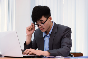 Surprised businessman with wide eyes hiding behind a laptop computer staring at the screen with a...