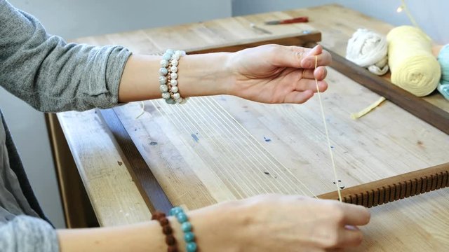 Weaving on a loom frame. Closeup woman's hands puts the thread in the frame for weaving.