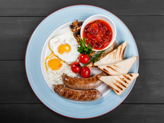 English breakfast - Fried eggs, beans, sausage, grilled tomatoes, mushrooms, toasted bread and sauce on plate on dark background