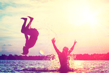 Glückliche junge Menschen laufen und springen am See beim Sonnenuntergang