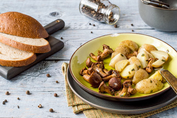 Fried mushrooms chanterelles and young potatoes on a round plate on an old wooden table. 