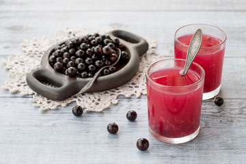 A fragrant berry drink in a glass and the fresh berries of black currant in a round wooden plate on...