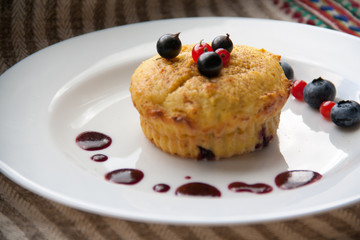 Homemade black currant cheese muffin with fresh berries and cherry sauce on white plate