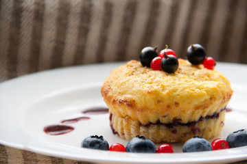Homemade black currant cheese muffin with fresh berries and cherry sauce on white plate