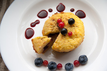 Homemade black currant cheese muffin with one slice. Fresh berries and cherry sauce on white plate