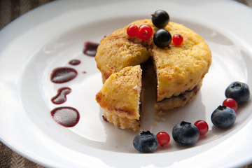Homemade black currant cheese muffin with one slice. Fresh berries and cherry sauce on white plate