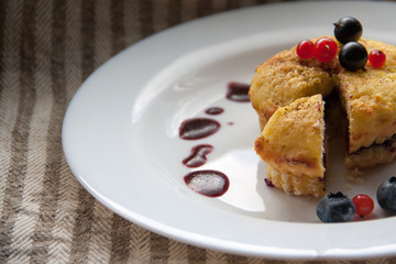 Homemade black currant cheese muffin with one slice. Fresh berries and cherry sauce on white plate