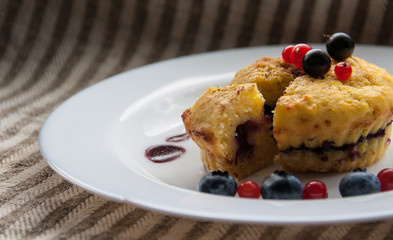 Homemade black currant cheese muffin with one slice. Fresh berries and cherry sauce on white plate