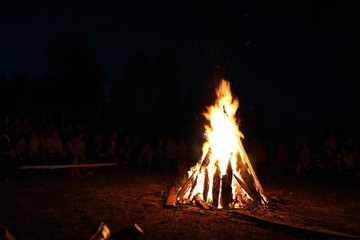 Blurred People sit at night around a bright bonfire