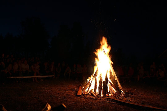 Blurred People sit at night around a bright bonfire