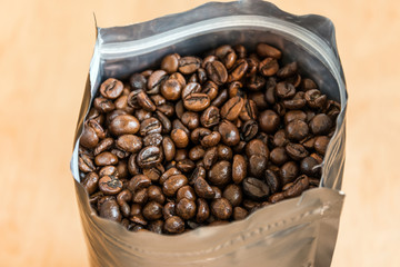 Coffee beans in a plastic foil package on wooden background. Roasted aromatic coffee top view.