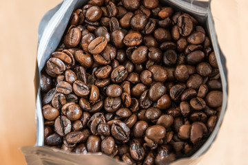Coffee beans in a plastic foil package on wooden background. Roasted aromatic coffee top view.