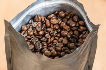 Coffee beans in a plastic foil package on wooden background. Roasted aromatic coffee top view.