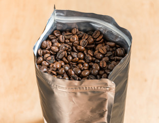 Coffee beans in a plastic foil package on wooden background. Roasted aromatic coffee top view.